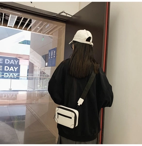 Street style view of a white mini box crossbody bag with black corners and a wide strap