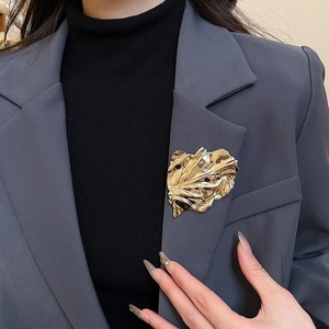 Detail of a golden irregular pleated leaf brooch pinned on a dark grey suit lapel