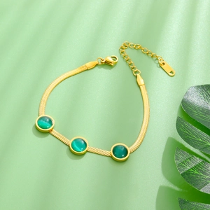 Détail d'un bracelet chaîne serpent dorée avec trois pierres œil-de-chat vertes sur fond doux