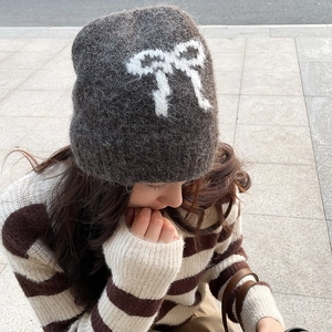 Detailed close-up showing soft grey knit texture and white plush bow on warm beanie hat