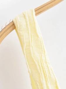 Detailed macro shot of pale yellow tree-textured pleated fabric on a wooden hanger