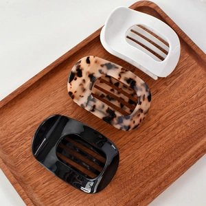 Detail view of acetate claw clips in white, tortoiseshell, and black on a wooden tray