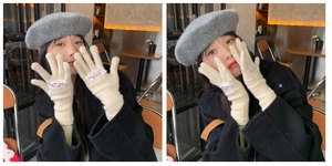 Detail of cream knit gloves with letter patch worn by a model in a cafe setting