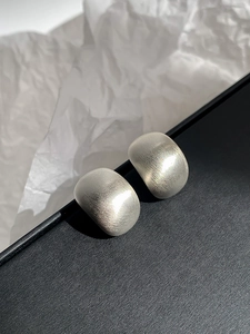 Macro shot of silver geometric earrings with a matte brushed metal finish on dark base