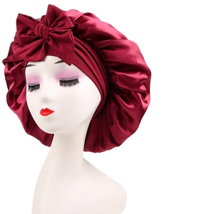 Close-up of a dark red satin sleep cap featuring a large decorative bow and elastic rim
