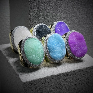 Multiple colorful crystal druzy rings with small crystals on rustic stone blocks