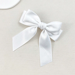 Detail of a white satin bow hair clip featuring smooth ribbon texture and elegant design