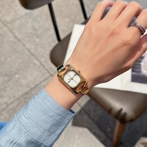 Elegant gold square watch with white dial on female wrist in cozy cafe setting