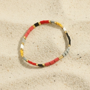 Detail of colorful Tila bead stretch bracelet with gold spacers on a sandy beach surface