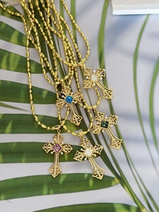 Detailed close-up of vintage gold cross necklaces with colorful gemstones on green leaves