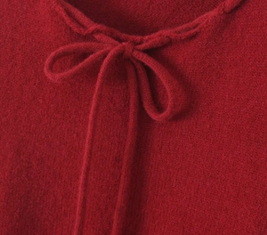 Detail eines roten Strickpullunders mit zarter Schleife am Ausschnitt und weicher Textur