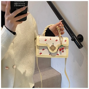 Detail of white handbag with cherry print, golden floral lock and braided handle