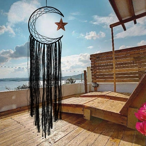 Detail of black moon dream catcher with woven mesh and tassels against a sunny sea view