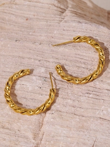 Macro detail of twisted gold-plated hoop earrings with textured finish on stone