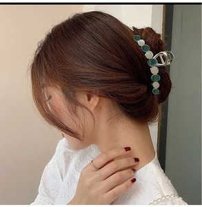 Detail of silver metal hair claw clip with green and beige round enamel accents in dark hair
