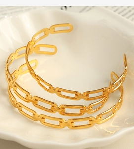 Detailed view of three stacked gold chain-style open bangles on a decorative tray