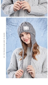 Close-up of gray knit winter earflap hat featuring thick cable knit and logo patch