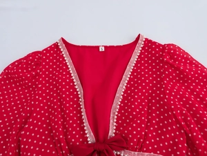 Dettaglio macro dell'abito rosso a pois con scollo a V, bordo di perle e accento di fiocco