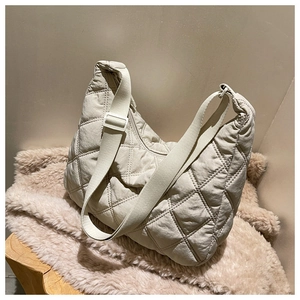 Detail of beige quilted nylon crossbody bag with wide strap on soft plush fabric