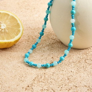Beaded necklace with turquoise and aquamarine stones on a ceramic vase and sandy background