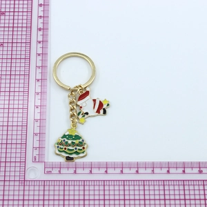 Detail of Christmas keychain with enamel Santa Claus and green tree charms on a pink mat