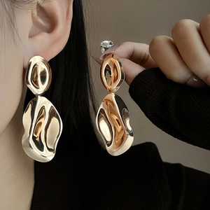Close-up of golden irregular wavy drop earrings on model showing metallic luster