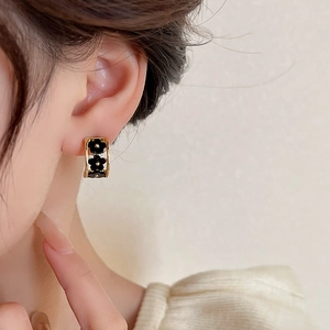 Detailed close-up of golden C-shaped earrings with black floral accents on model's ear