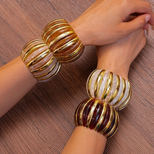 Detail of layered gold metal and tinted acrylic resin elastic bracelets on model wrist