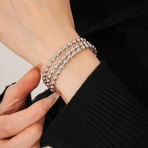 Dettaglio di un bracciale a tre strati con perline d'argento indossato al polso su maglia nera