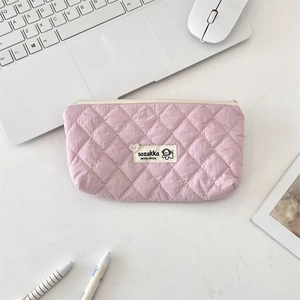 Detailed close-up of pink quilted makeup bag with rhombic stitching and white logo tag