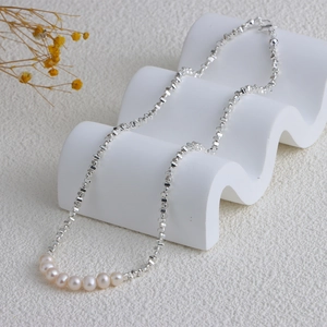 Detail of silver irregular square chain with seven round white pearls on white wave stand
