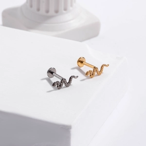 Detail of snake-shaped piercing studs in gold and silver finishes on a white pedestal