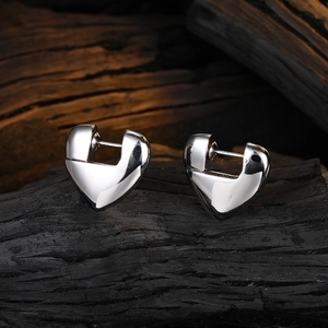 Polished silver heart earrings on dark textured wood base for a minimalist aesthetic
