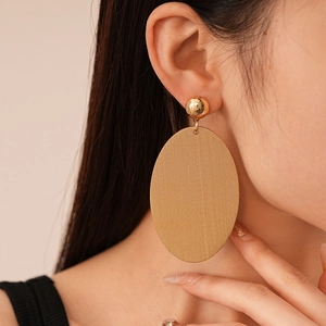 Detail of large gold oval earring with brushed metal texture worn by a fashion model