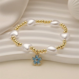 Close-up of heart pearl bracelet with light blue floral charm and gold metal beads
