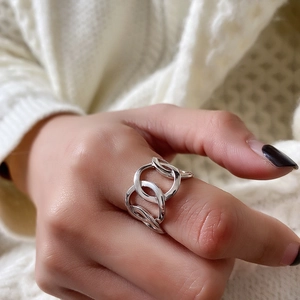 Close-up of interlocking hollow silver rings worn on finger with knit sweater background