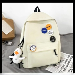 Off-white canvas school backpack with colorful badges and a plush duck charm for students