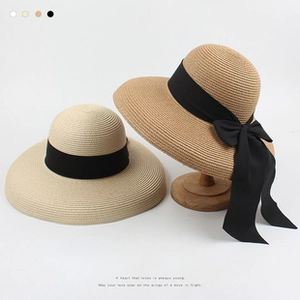 Detail of beige and light brown straw sun hats with black ribbons on wooden stand