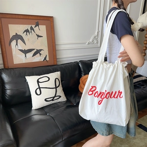 Detail of white canvas tote bag with red Bonjour text and drawstring closure