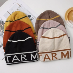 Flat lay of colorful knitted beanies with letter patches in orange, yellow and pink