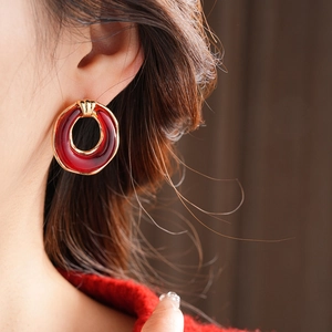 Close-up of elegant gold-rimmed red resin earrings worn to showcase the sleek round design