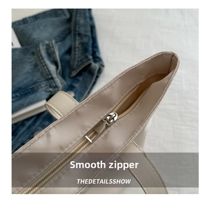 Close-up of a smooth silver metal zipper on a cream nylon tote bag with clean stitching