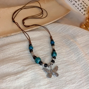 Macro detail of vintage butterfly pendant with turquoise beads and brown woven cord