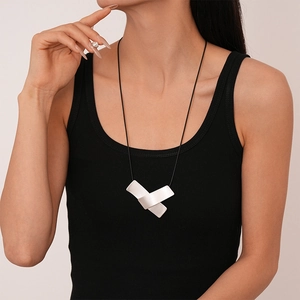Close-up of geometric silver metal pendant on black cord worn by a model in dark tank top