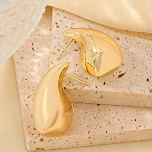 Macro view of teardrop gold stud earrings on beige stone and yellow silk fabric