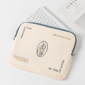 Detail of off-white laptop sleeve featuring blue zipper and intricate quote embroidery