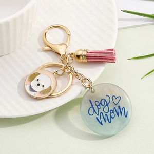 Detail view of Dog Mom glitter keychain with Bichon charm and pink tassel on ceramic plate