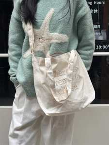 Detail of embroidered lettering on an off-white canvas tote bag with adjustable straps