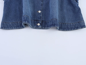 Detailed close-up of dark blue denim jacket hem with metallic buttons and washed texture
