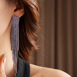 Vue rapprochée de longues boucles d'oreilles à pompons violets avec strass sur modèle